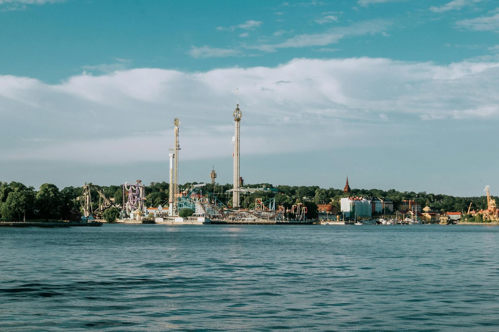 Gröna Lunds nöjespark från vattnet, med höga åkattraktioner och trädklädd kust.
